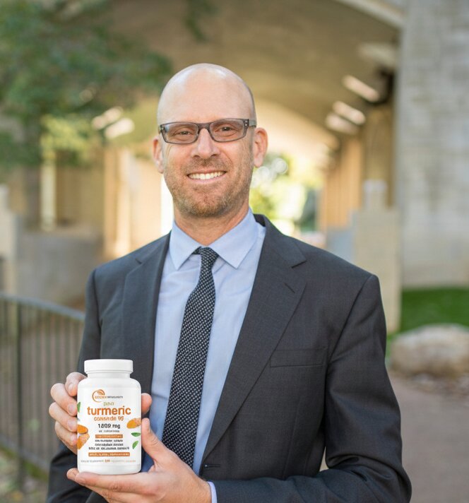 Man in a suit holding a bottle of turmeric supplements outdoors.