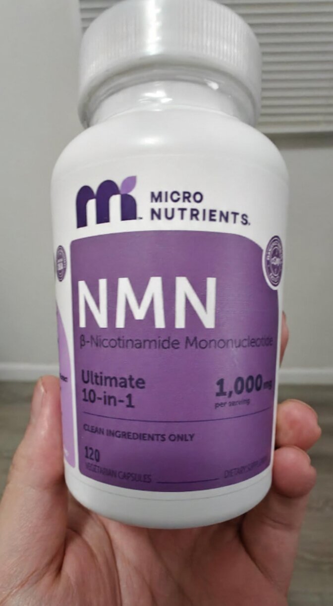 Hand holding a bottle of NMN supplements with a white background