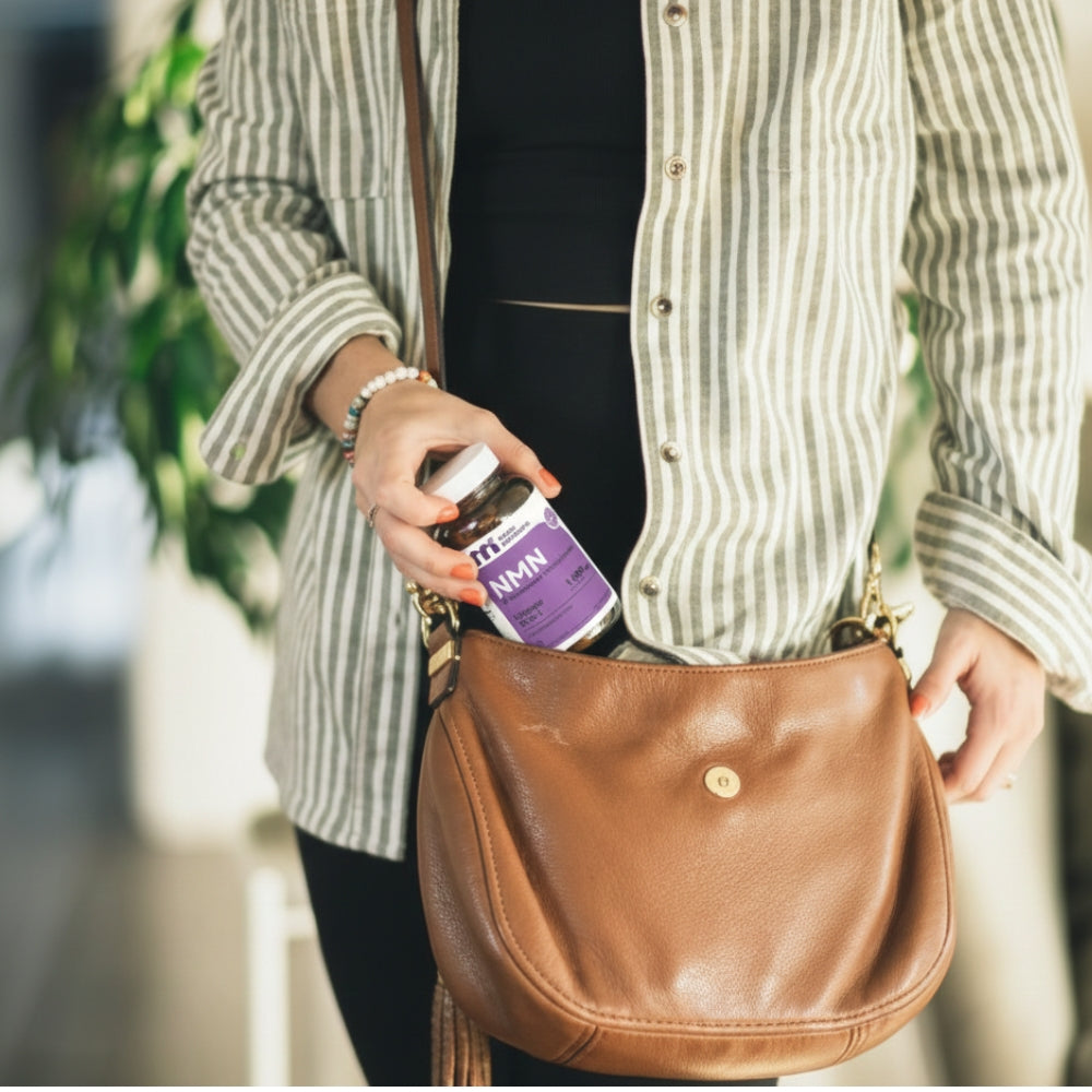 Person holding a brown leather handbag with a purple nmn bottle inside, blurred background