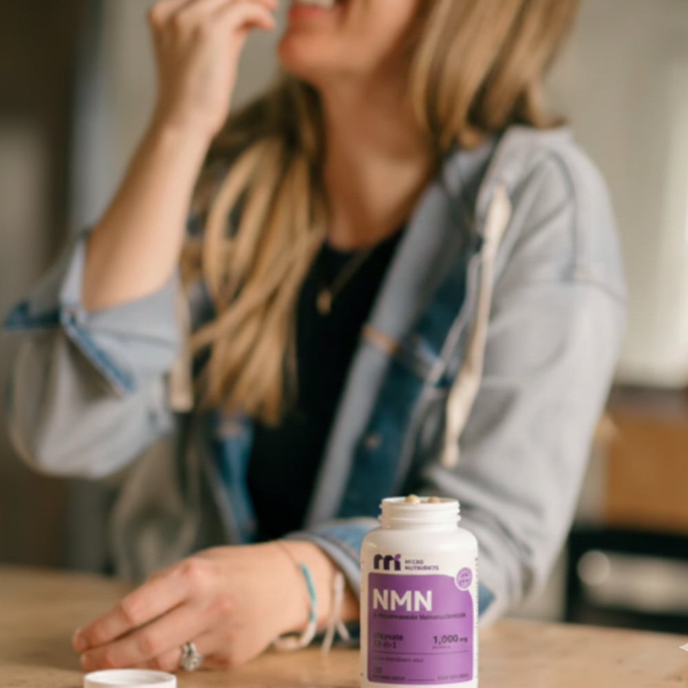 Woman sitting at a table with a bottle of NMN supplements in the foreground.