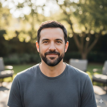 Man with a beard wearing a gray shirt outdoors with greenery in the background