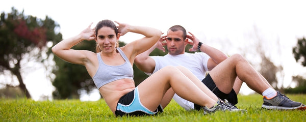 Two people exercising outdoors on grass with trees in the background