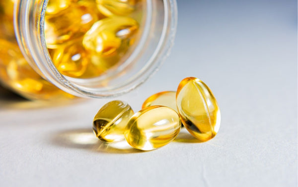 Yellow capsules spilling out of a glass jar on a light gray background