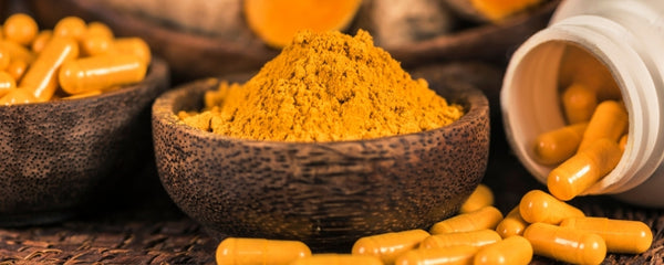 Turmeric powder in a wooden bowl with turmeric capsules around it.
